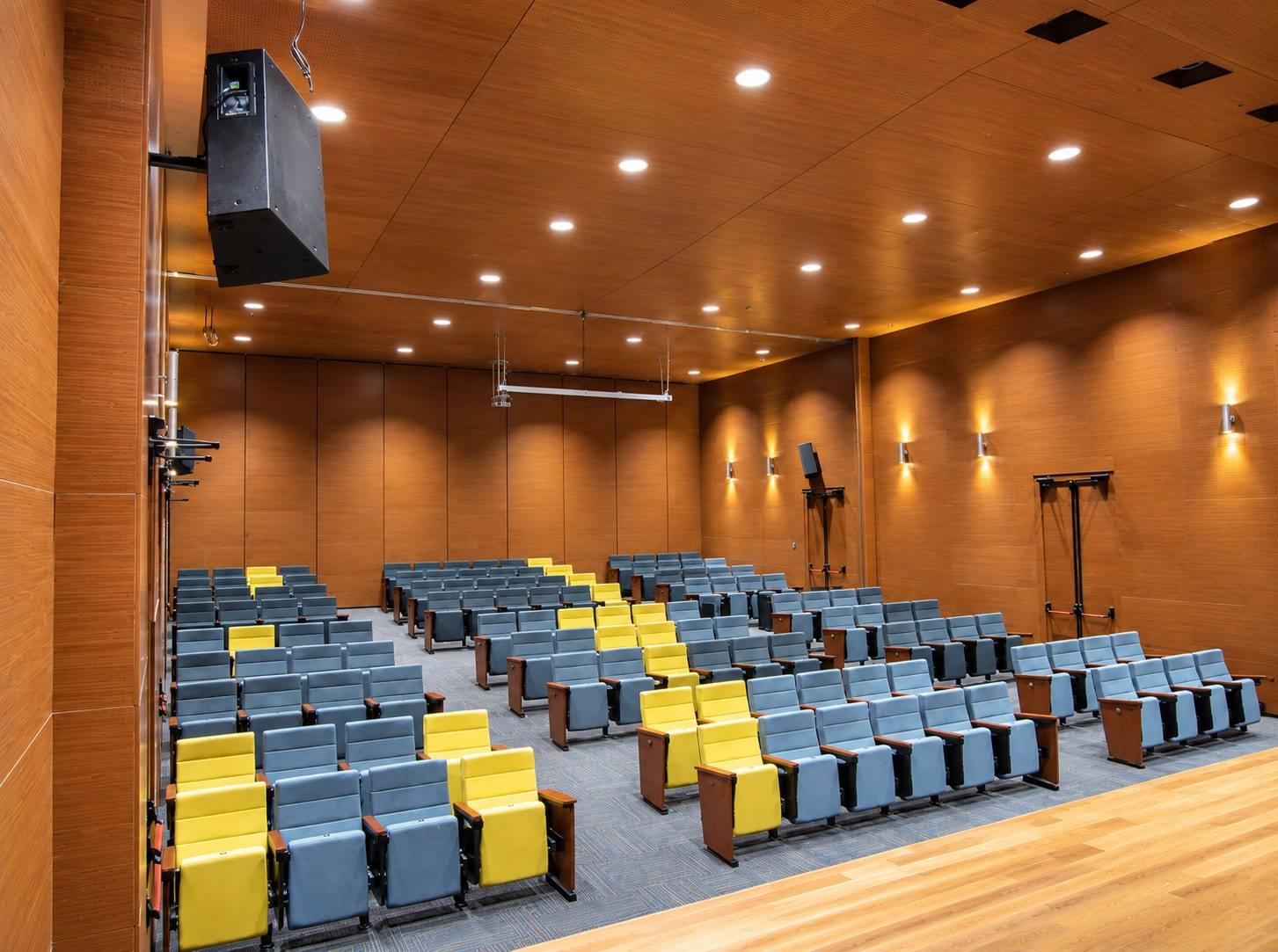 Auditorio revestido en madera con butacas azules y amarillas.